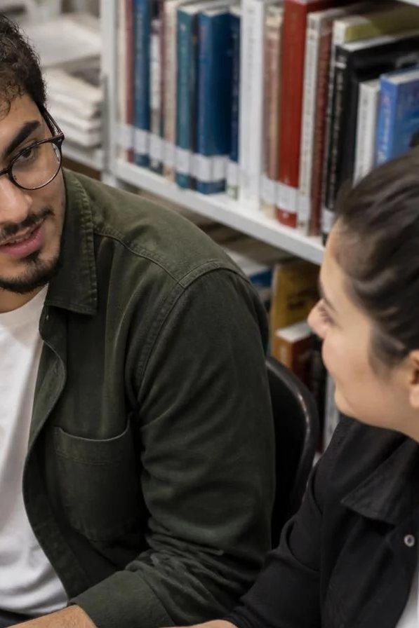 Duas participantes de pé conversando no corredor entre prateleiras de livros
